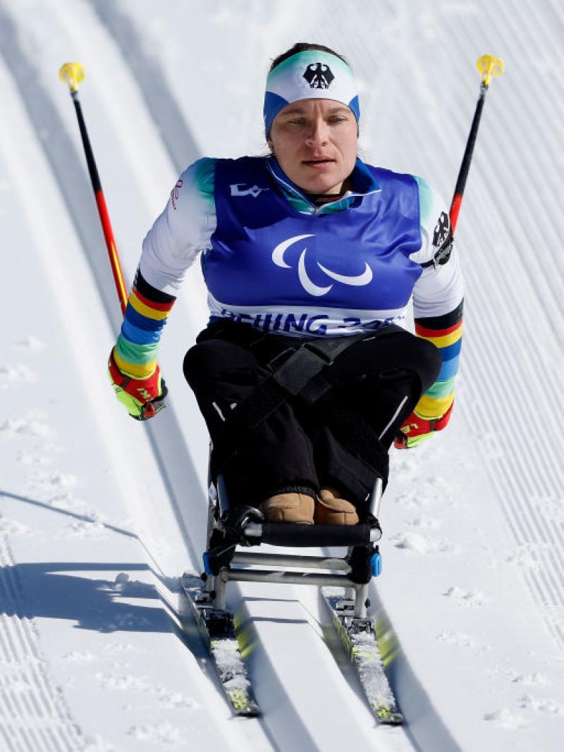A female sit-skiing athlete is racing down hill in the cross-country segment of a Para biathlon event